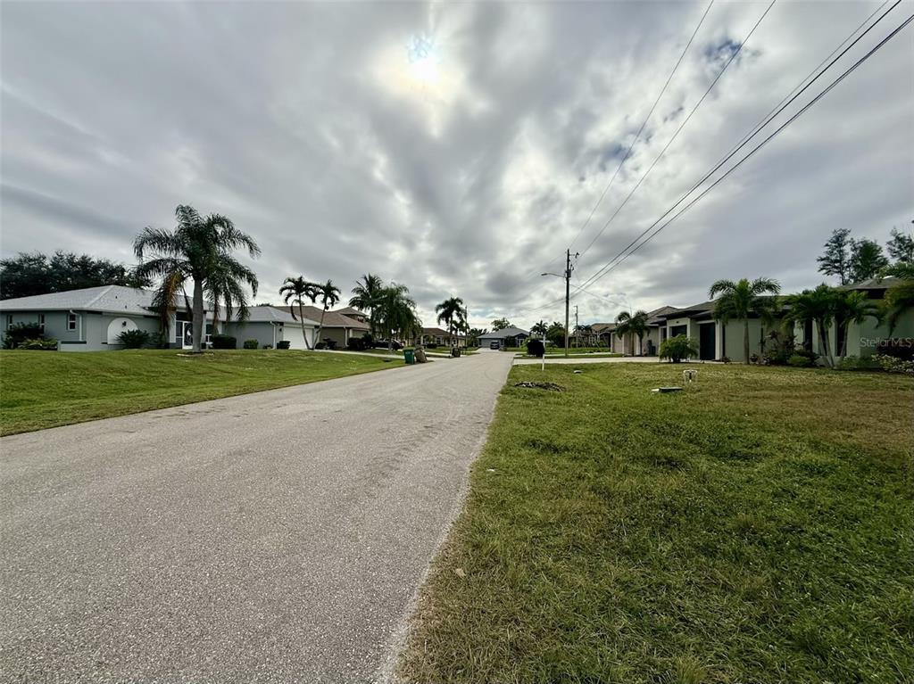 A residential street lined with houses, palm trees, and grassy lawns under a cloudy sky — 1414 SW 1ST PLACE, CAPE CORAL, FL