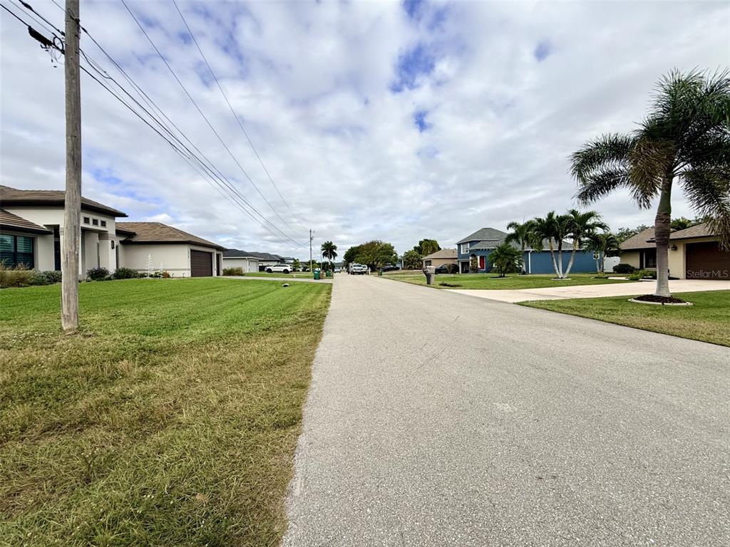 A residential street with houses, manicured lawns, and palm trees under a cloudy sky — 1414 SW 1ST PLACE, CAPE CORAL, FL
