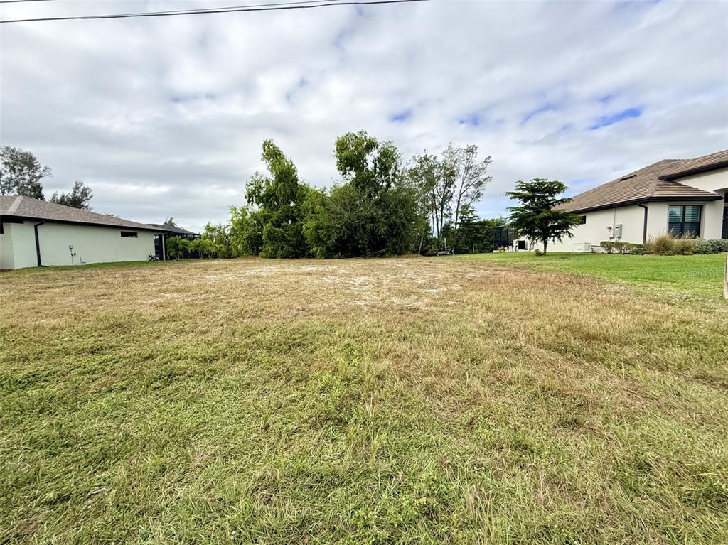 A vacant grassy lot sits between two residential houses under a cloudy sky — 1414 SW 1ST PLACE, CAPE CORAL, FL