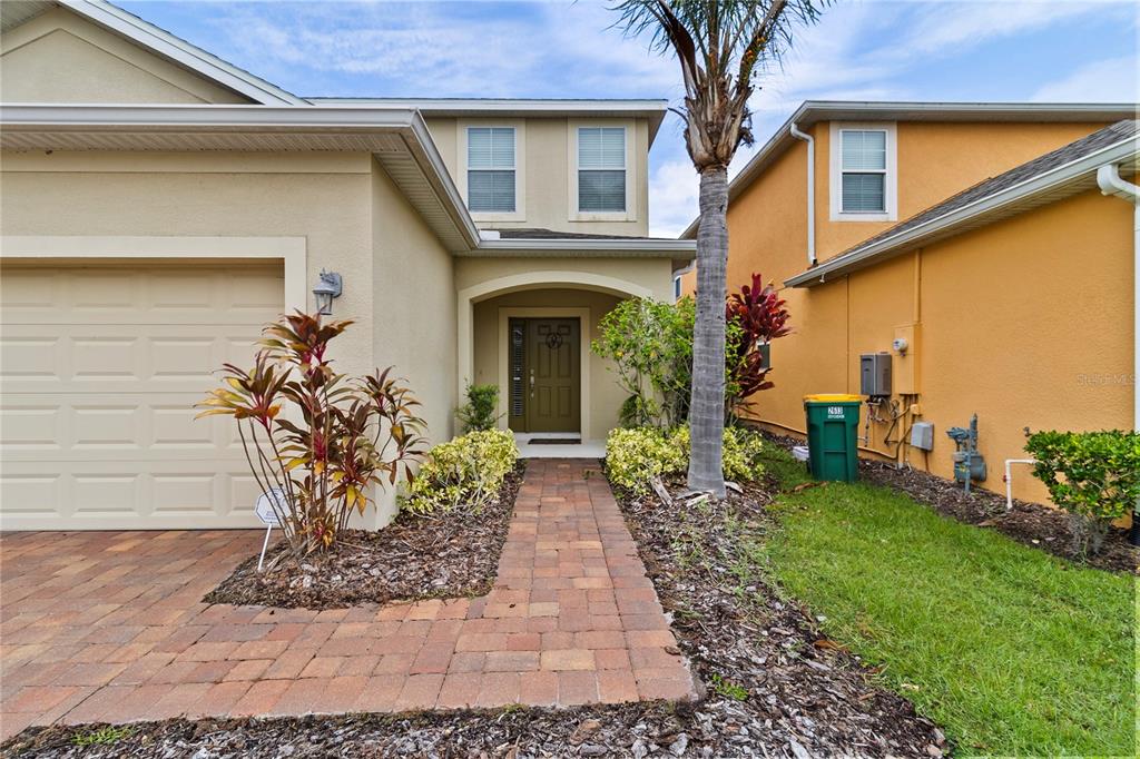 A beige house exterior features a brick walkway leading to a dark green front door — 2615 SANTOSH COVE, KISSIMMEE, FL