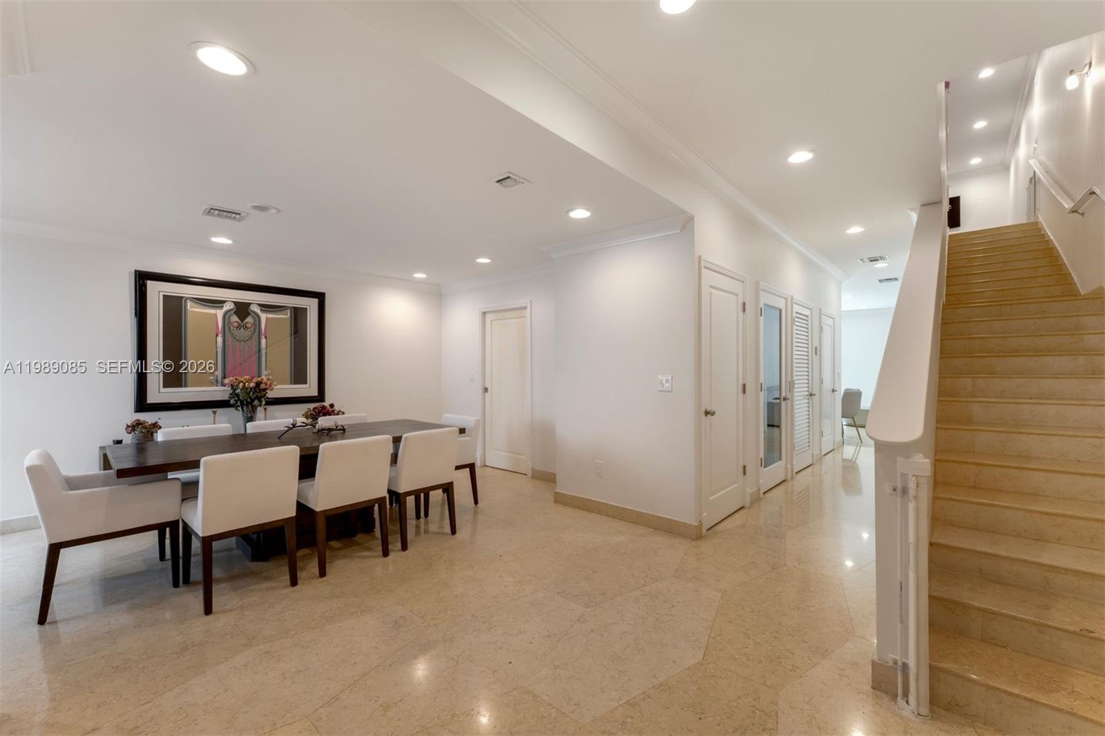 A dining area with a long table and chairs sits beside a staircase with tile flooring — 1566 NE Quayside Ter # D14, Miami FL 33138, MIAMI, FL