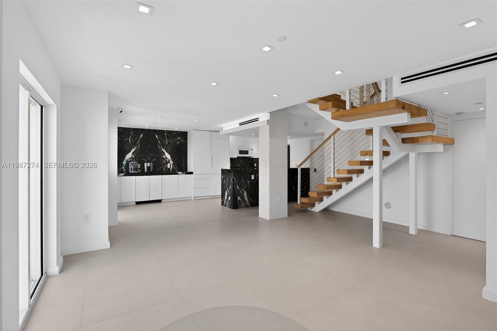 A modern open-plan living area features a black marble kitchen, light tile floors, and stairs — 120 Jefferson Ave # 12009, Miami Beach FL 33139, MIAMI BEACH, FL