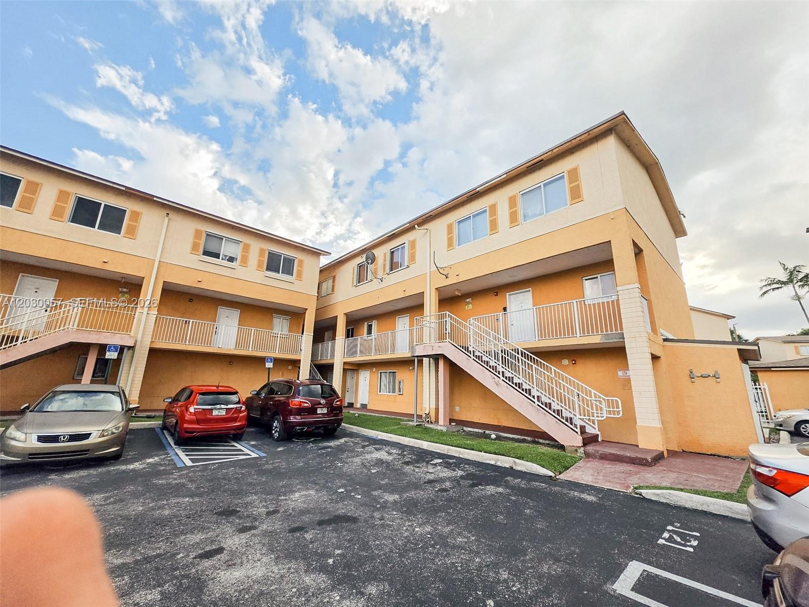 An exterior view of a two-story apartment building with orange stucco walls and outdoor staircases — 6235 Kendale Lakes Cir # 236, Miami FL 33183, MIAMI, FL