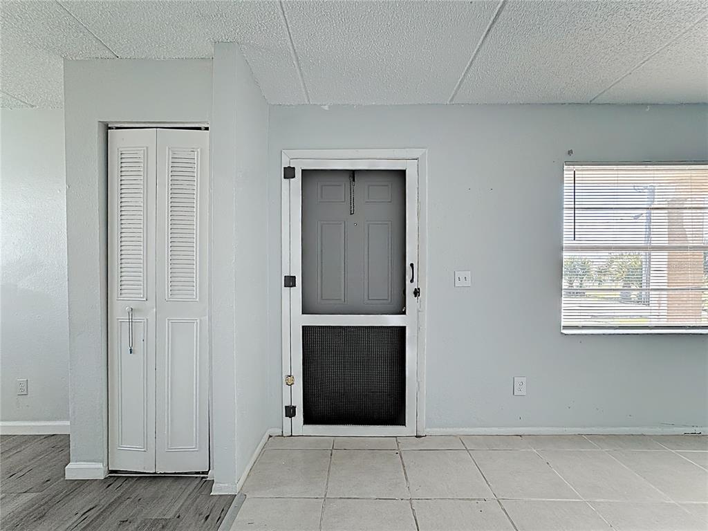 A room with light-colored tile flooring, a white louvered closet door, and a screen door — 694 MICHIGAN COURT UNIT 3, ST CLOUD, FL