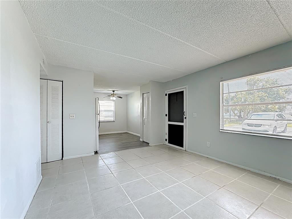 A living room with light-colored tile flooring leads into a kitchen with wood-look flooring — 694 MICHIGAN COURT UNIT 3, ST CLOUD, FL
