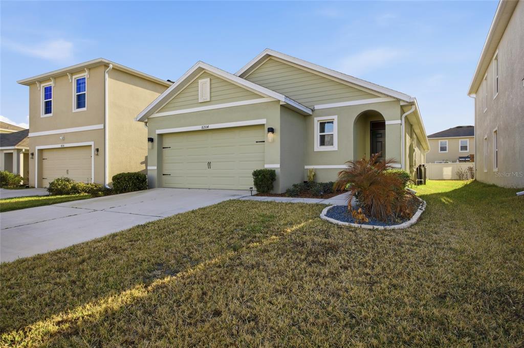 A light green single-story house with a two-car garage and a small front yard — 8204 PELICAN REED CIRCLE, WESLEY CHAPEL, FL