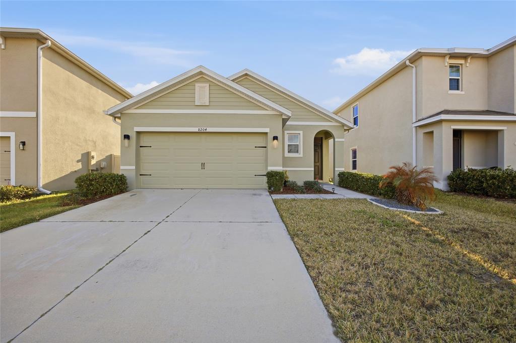 A single-story house with a beige garage, light green siding, and a concrete driveway — 8204 PELICAN REED CIRCLE, WESLEY CHAPEL, FL