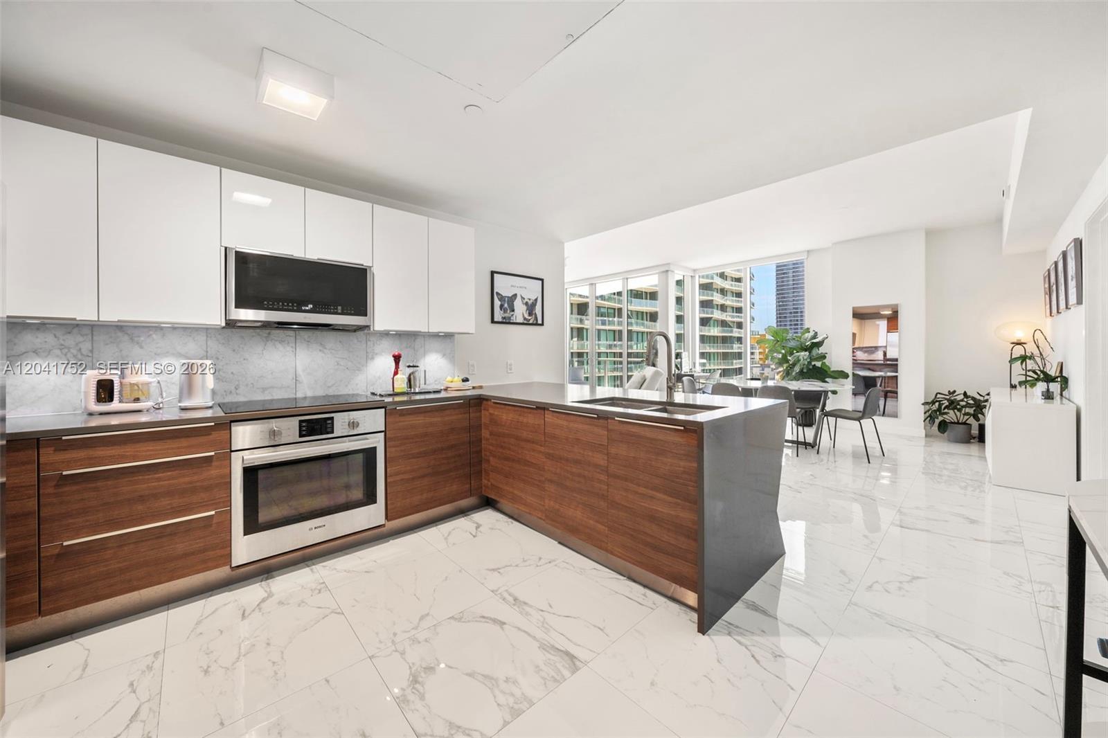A modern kitchen features white upper cabinets, wood-grain lower cabinets, and white marble-patterned tile floors — 601 NE 27th St # 1001, Miami FL 33137, MIAMI, FL