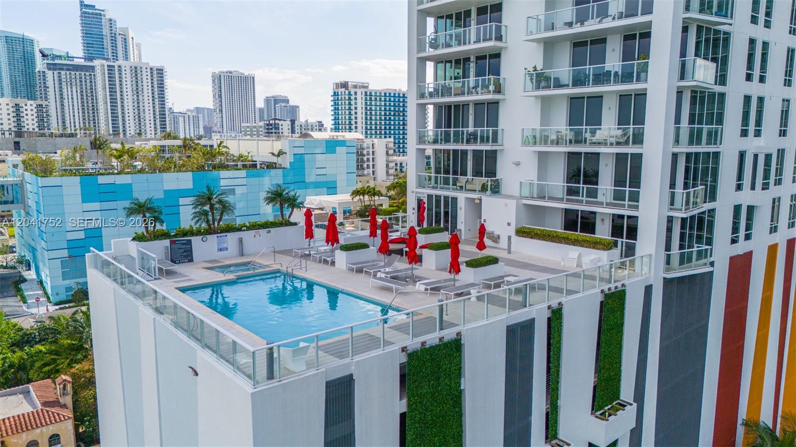 An elevated outdoor swimming pool deck features lounge chairs, red umbrellas, and vertical garden walls — 601 NE 27th St # 1001, Miami FL 33137, MIAMI, FL