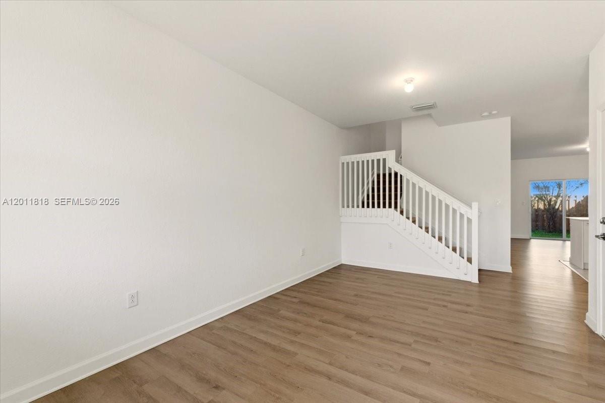 An empty room features white walls, light wood-look flooring, and a white staircase railing — 12865 NW 24th Ave, Miami FL 33167, MIAMI, FL