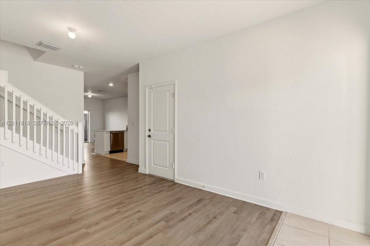 An interior view shows a living area with wood-look flooring, a staircase, and a doorway — 12865 NW 24th Ave, Miami FL 33167, MIAMI, FL