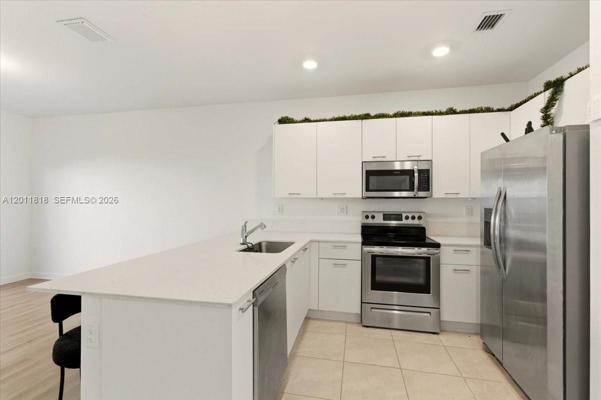 A modern kitchen features white cabinets, stainless steel appliances, and a white quartz island — 12865 NW 24th Ave, Miami FL 33167, MIAMI, FL