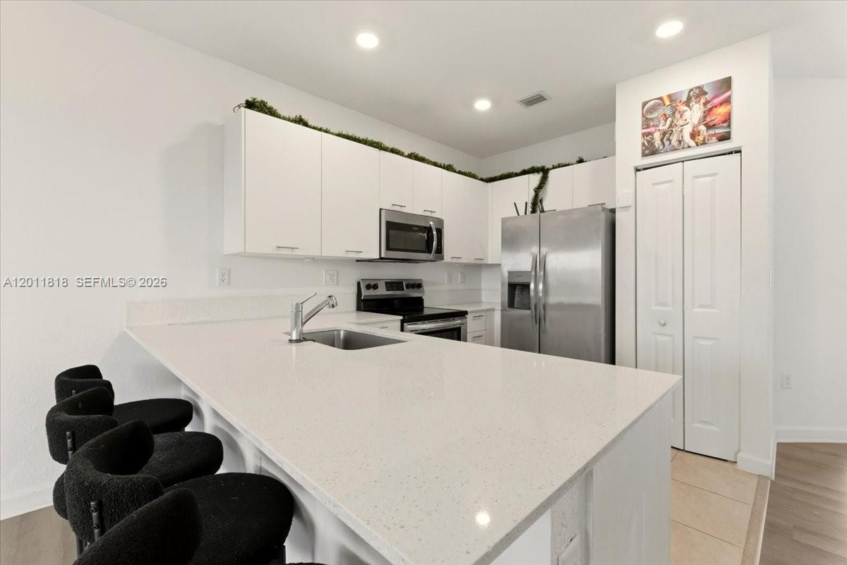 A modern kitchen features white cabinets, stainless steel appliances, and a white quartz island — 12865 NW 24th Ave, Miami FL 33167, MIAMI, FL