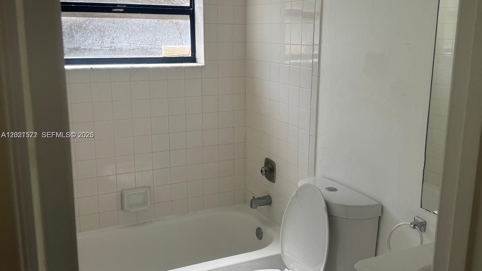 A bathroom features a white bathtub with tiled walls, a toilet, and a window — 2715 W 66th St # 21, Hialeah FL 33016, HIALEAH, FL