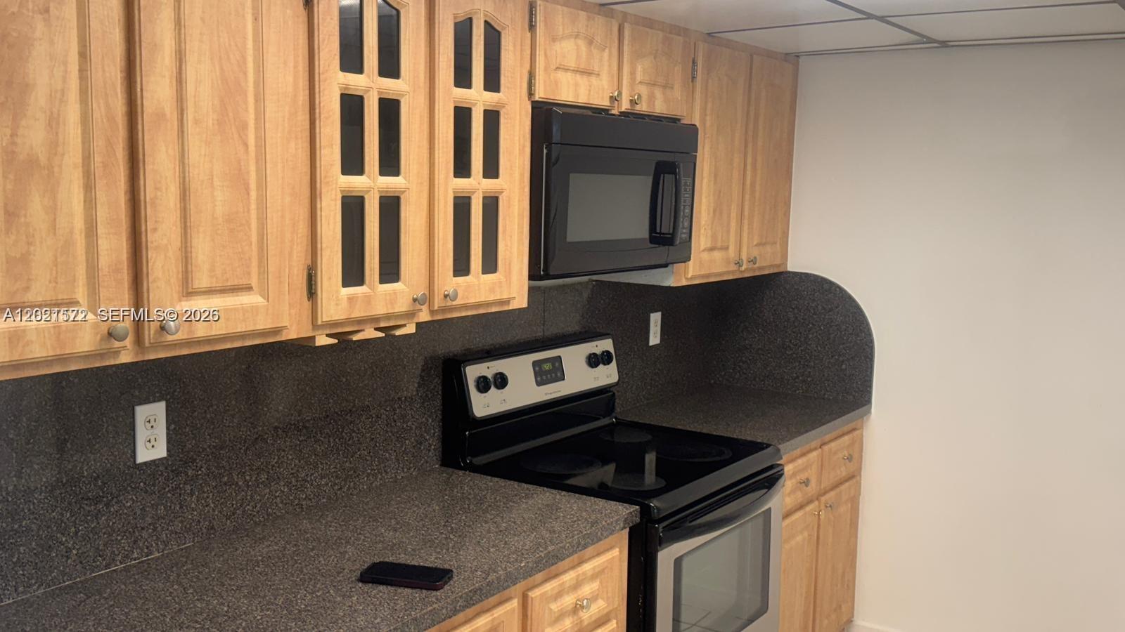 A kitchen features light wood cabinets, black appliances, and dark speckled laminate countertops — 2715 W 66th St # 21, Hialeah FL 33016, HIALEAH, FL