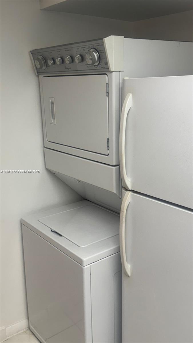 A white stacked laundry unit sits next to a white refrigerator in a small space — 2715 W 66th St # 21, Hialeah FL 33016, HIALEAH, FL