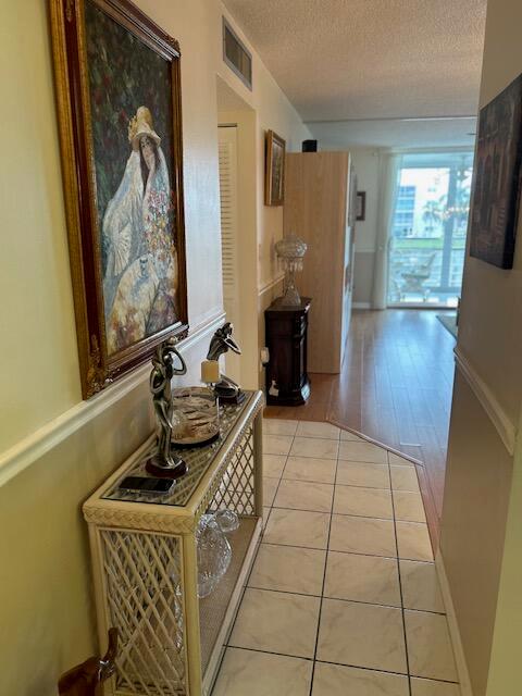 A hallway features a wicker console table, a large framed painting, and tile flooring — 324 SE 10th Street # 207, Dania Beach FL 33004, DANIA BEACH, FL