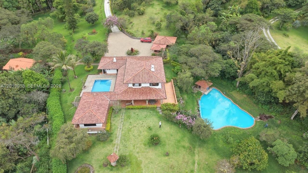An aerial view shows a house with a red tile roof, two pools, and gardens — NA Via Guadaleg, FL