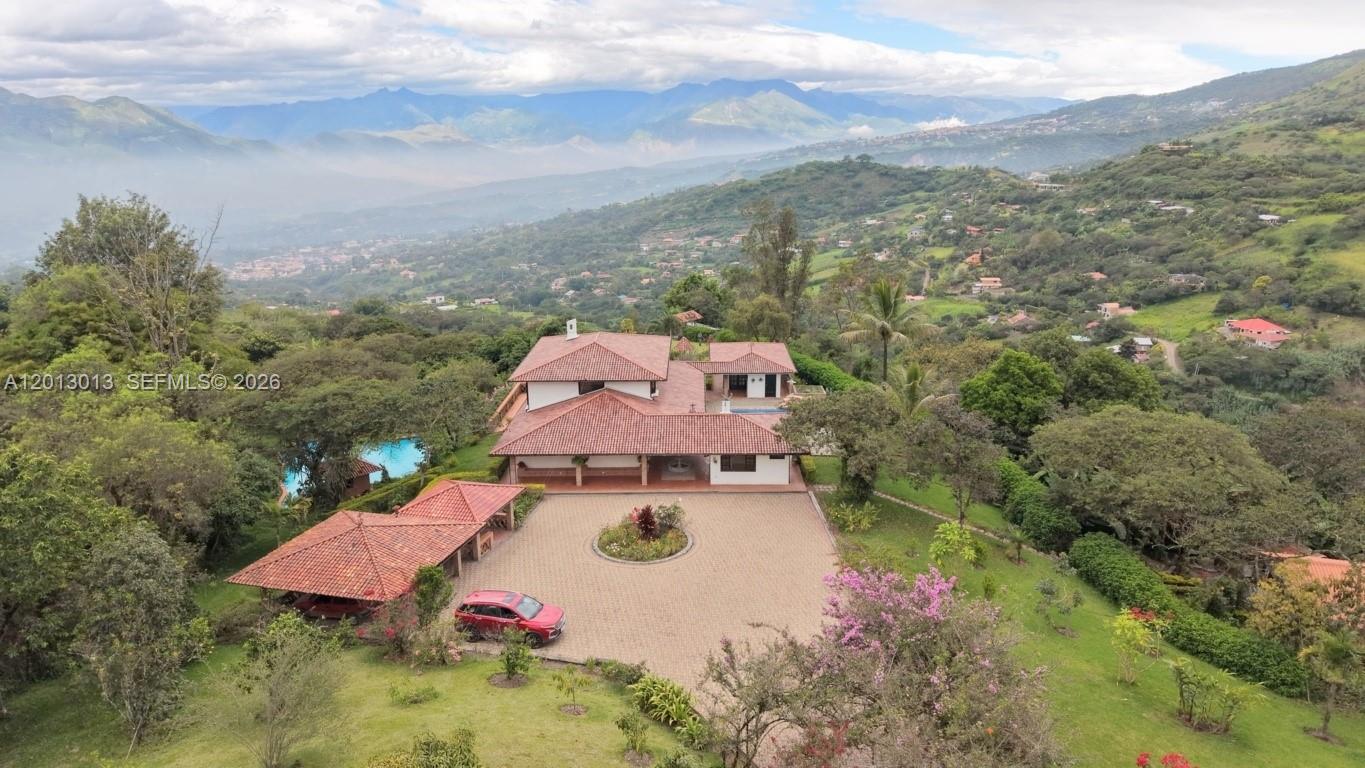 An aerial view shows a house with a tiled roof, pool, and driveway on a hillside — NA Via Guadaleg, FL