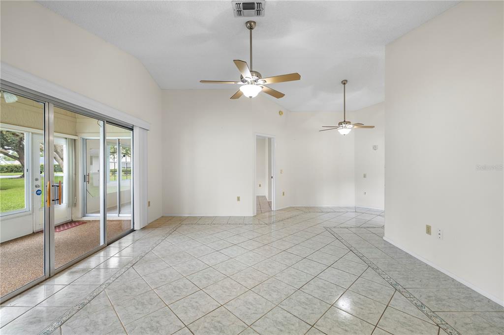 An empty room with vaulted ceilings, tile flooring, two ceiling fans, and sliding glass doors — 4739 CARRINGTON COURT, NEW PORT RICHEY, FL