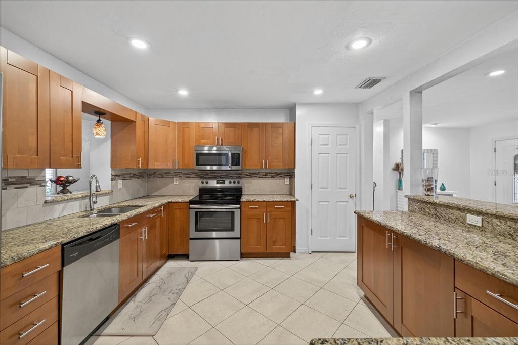 A kitchen with wood cabinets, granite countertops, stainless steel appliances, and light-colored tile flooring — 420 LEWIS BOULEVARD SE, ST PETERSBURG, FL