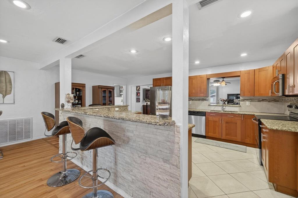 A kitchen with wood cabinets and granite countertops features a stone-faced breakfast bar with stools — 420 LEWIS BOULEVARD SE, ST PETERSBURG, FL
