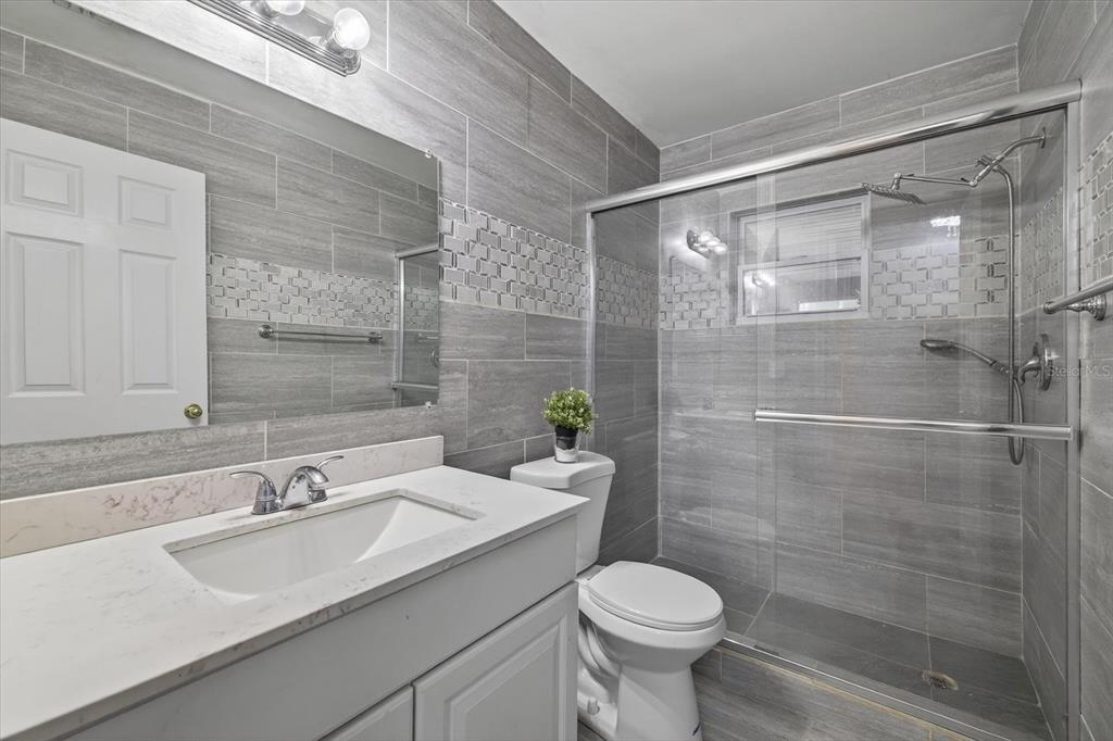 A bathroom features gray tiled walls, a white vanity, a toilet, and a glass shower enclosure — 420 LEWIS BOULEVARD SE, ST PETERSBURG, FL