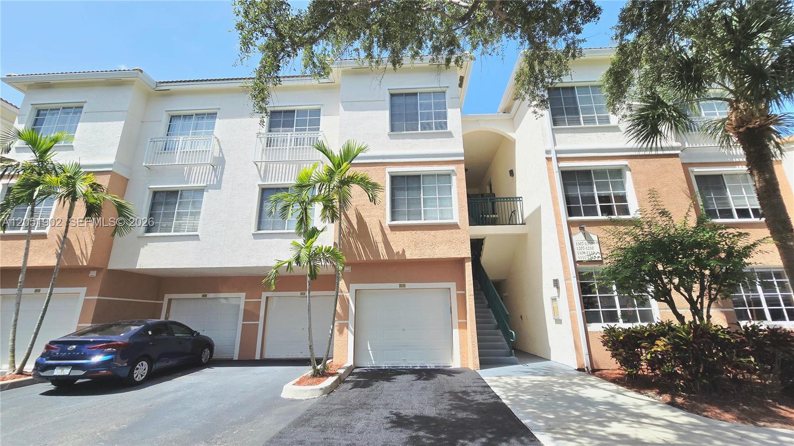 The exterior of a three-story residential building features stucco walls, multiple garages, and palm trees — 1307 E Myrtlewood Cir E # 1307, Palm Beach Gardens FL 33418, PALM BEACH GARDENS, FL