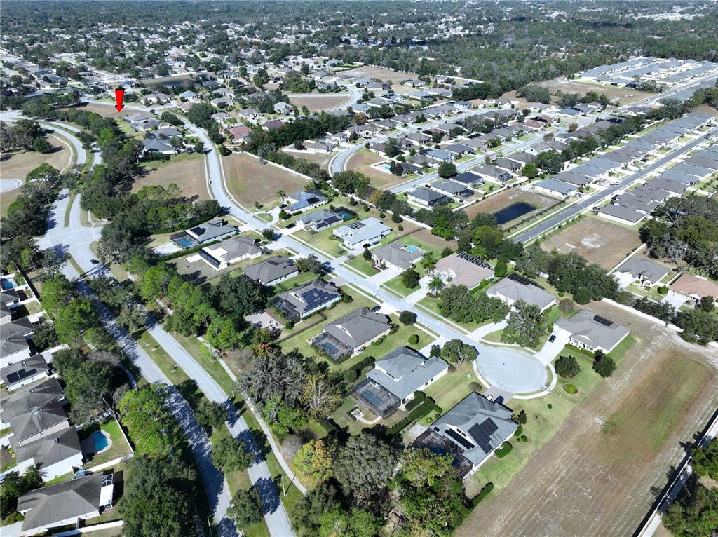 An aerial view shows a suburban neighborhood with houses, streets, and green spaces — 13822 BASSINGTHORPE DRIVE, SPRING HILL, FL
