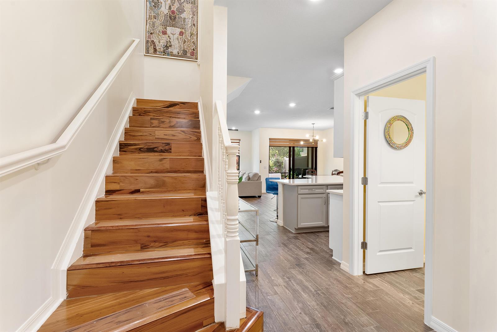 A wooden staircase leads to an upper level beside a doorway and an open kitchen — 4846 San Fratello Circle, FL 33467, FL