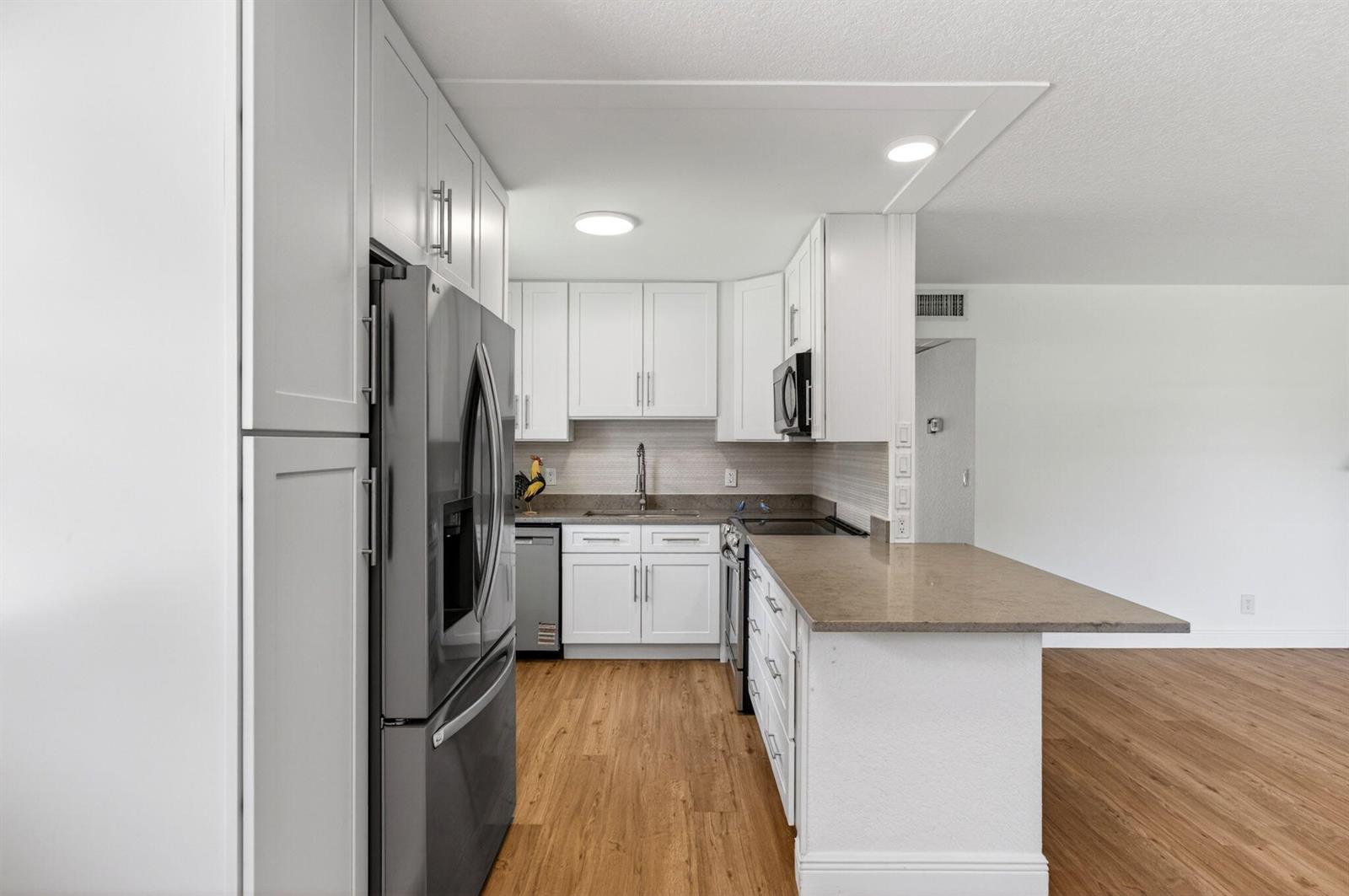 A kitchen features white cabinets, stainless steel appliances, and a peninsula with a stone countertop — 221 Waterford # J, Delray Beach FL 33446, DELRAY BEACH, FL
