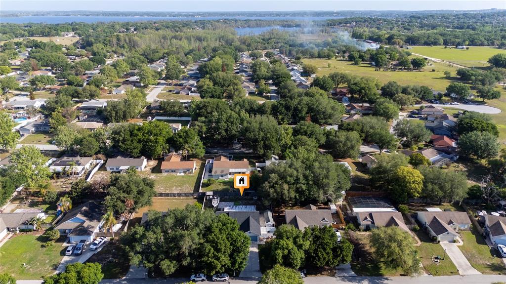 An aerial view shows a suburban neighborhood with single-family homes, mature trees, and a lake — 10618 REAGANS RUN DRIVE, CLERMONT, FL