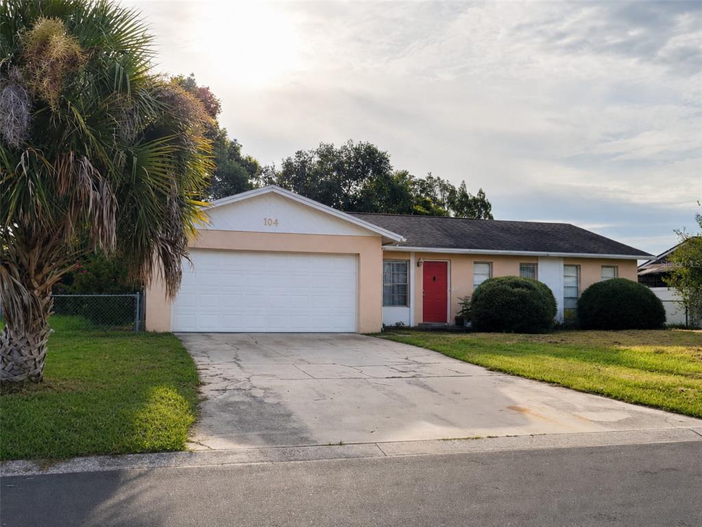 A single-story house with a peach-colored exterior, a red front door, and a two-car garage — 104 MORELIA LANE, KISSIMMEE, FL