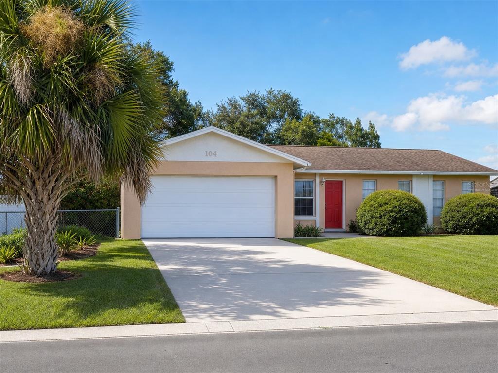 A single-story house with a white garage door, red front door, and a palm tree — 104 MORELIA LANE, KISSIMMEE, FL