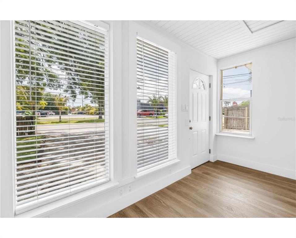 A bright room features white walls, wood-look flooring, two large windows with blinds, and a door — 110 NE MONROE CIRCLE N UNIT 1, ST PETERSBURG, FL