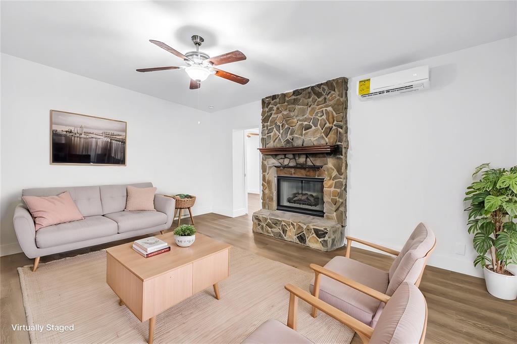 A living room features a stone fireplace, wood flooring, a ceiling fan, and virtual furniture — 110 NE MONROE CIRCLE N UNIT 1, ST PETERSBURG, FL
