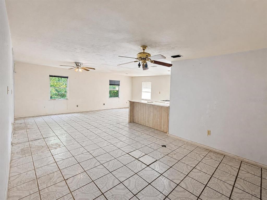 An open-concept room features white tiled floors, two ceiling fans, and a kitchen peninsula — 6806 SE 215TH STREET, HAWTHORNE, FL
