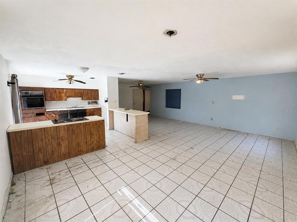 An open-concept kitchen and living area features tiled floors, wood cabinets, and two ceiling fans — 6806 SE 215TH STREET, HAWTHORNE, FL