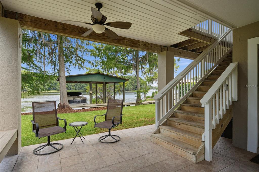 A covered patio features tile flooring, two chairs, and a wooden staircase leading upstairs — 6610 S MERLEING LOOP, FLORAL CITY, FL