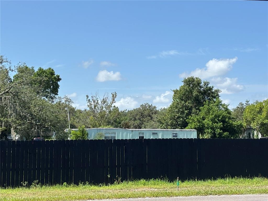 A light-colored mobile home sits behind a tall black wooden privacy fence — 10416 HUDSON AVENUE, HUDSON, FL
