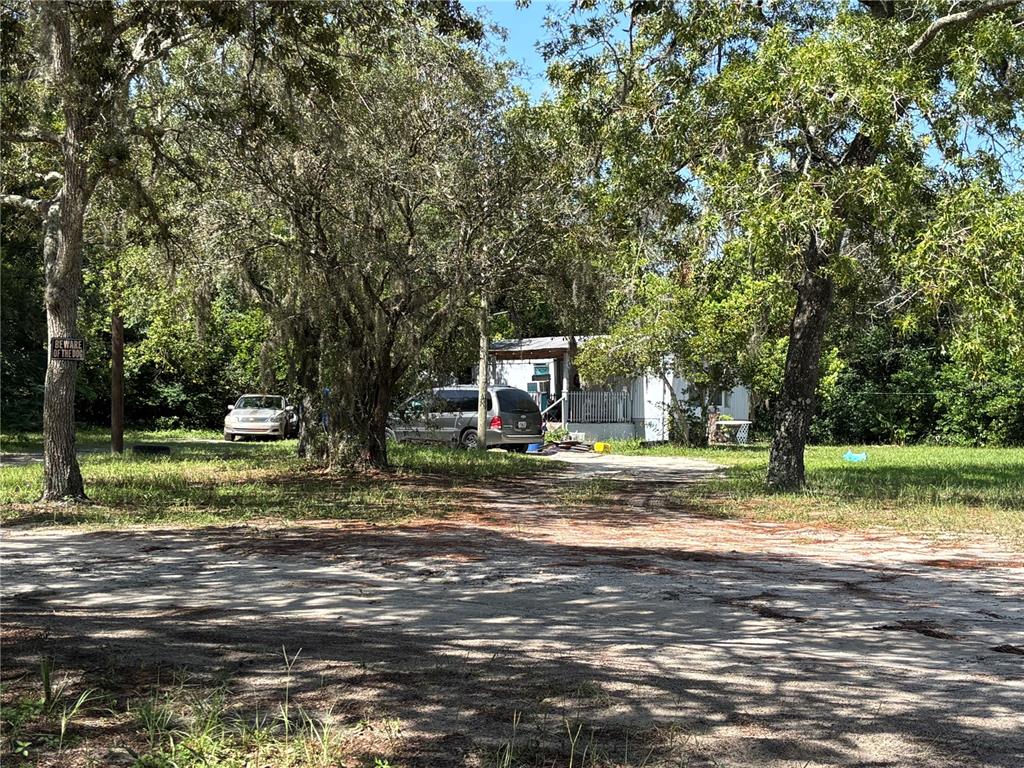 A white mobile home sits on a wooded lot with a dirt driveway and two vehicles — 10416 HUDSON AVENUE, HUDSON, FL