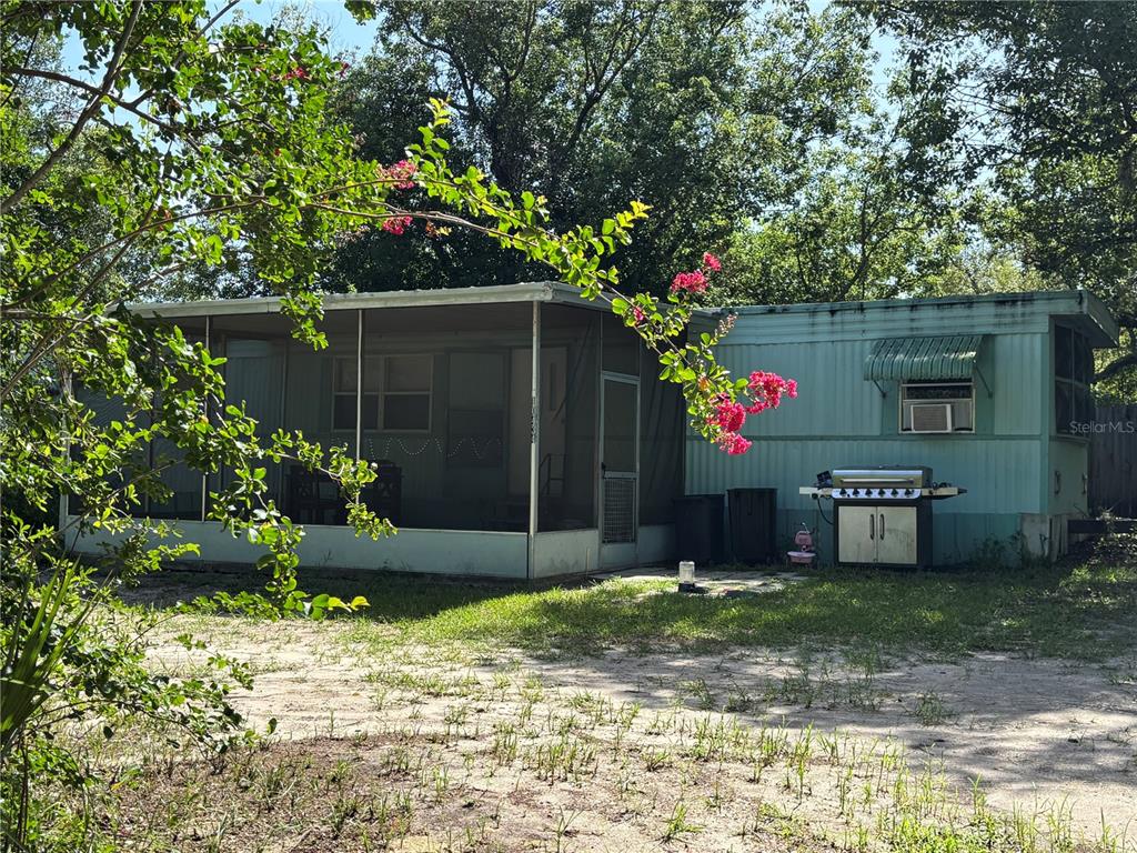 A mobile home with a screened-in porch and a grill sits on a sandy lot — 10416 HUDSON AVENUE, HUDSON, FL