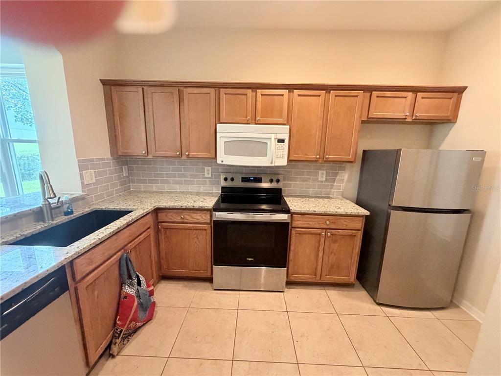 A kitchen features wood cabinets, granite countertops, stainless steel appliances, and a subway tile backsplash — 1146 GRANTHAM DRIVE, SARASOTA, FL