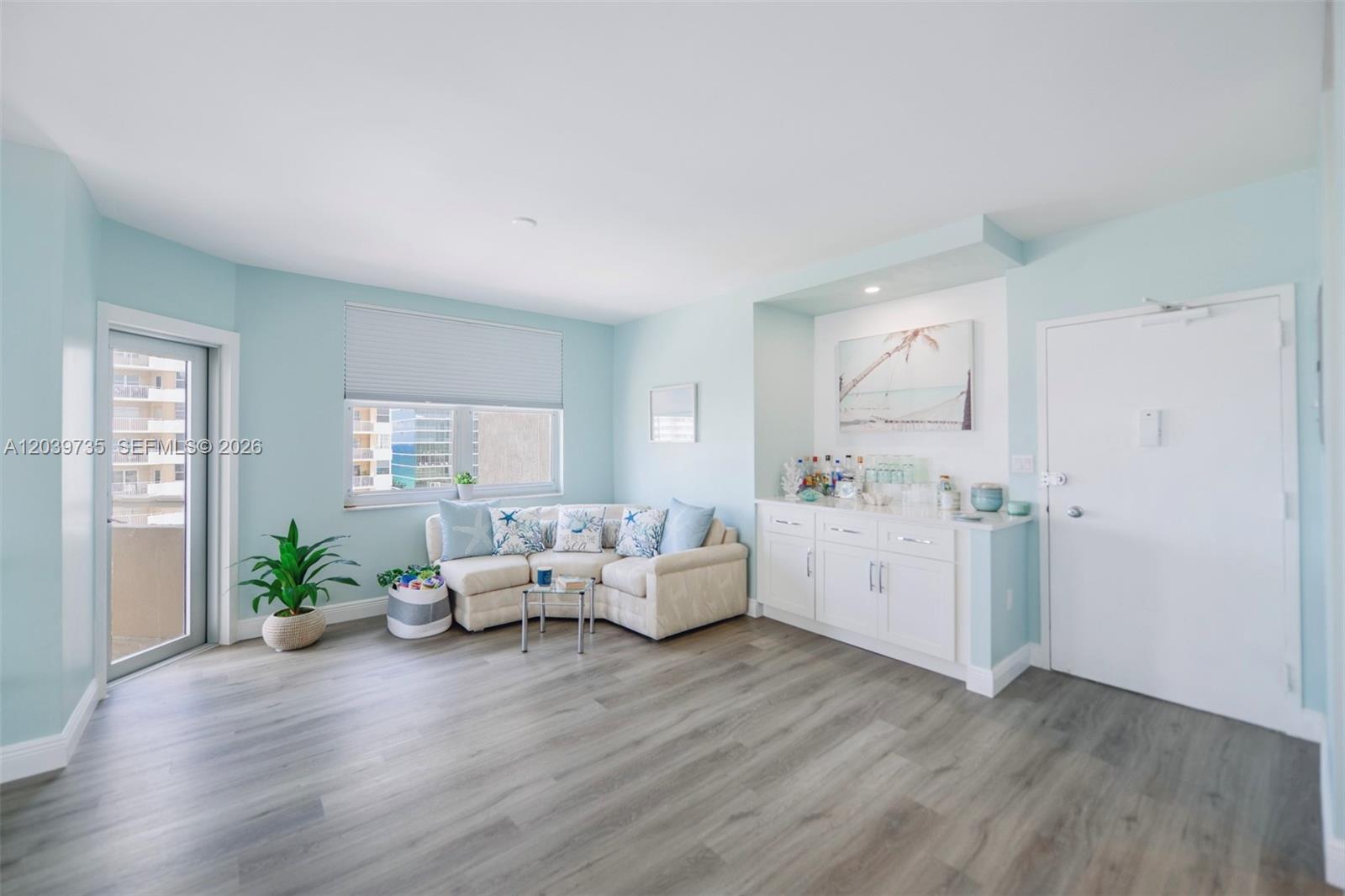 A living room features light blue walls, wood-look flooring, a sectional sofa, and a wet bar — 1985 S Ocean Dr # 8P, Hallandale Beach FL 33009, HALLANDALE BEACH, FL