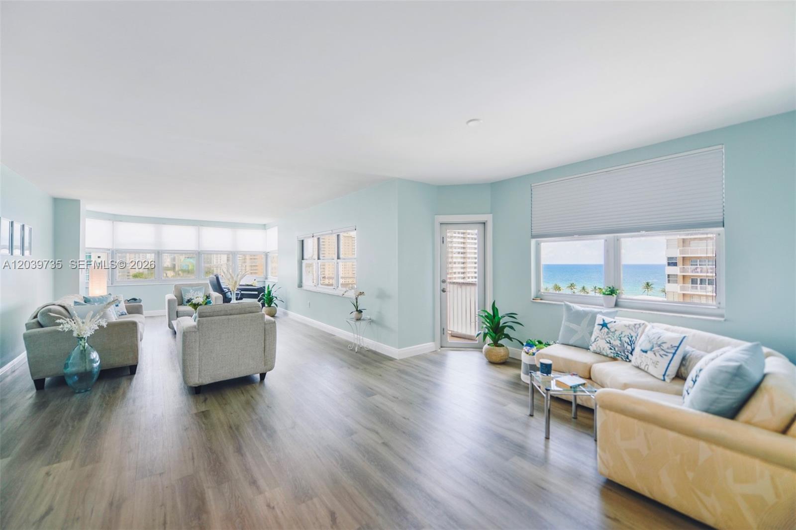 A bright, open-concept living room features light blue walls, wood-look flooring, and ocean views — 1985 S Ocean Dr # 8P, Hallandale Beach FL 33009, HALLANDALE BEACH, FL