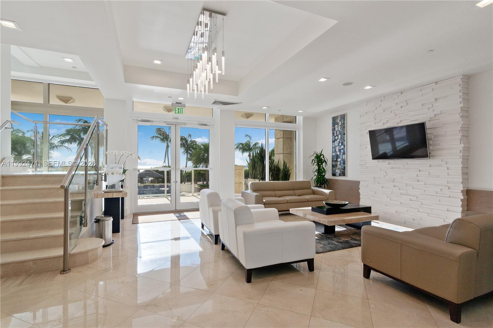 A modern lobby features white leather seating, a stone accent wall, and a glass staircase — 4779 Collins Ave # 808, Miami Beach FL 33140, MIAMI BEACH, FL