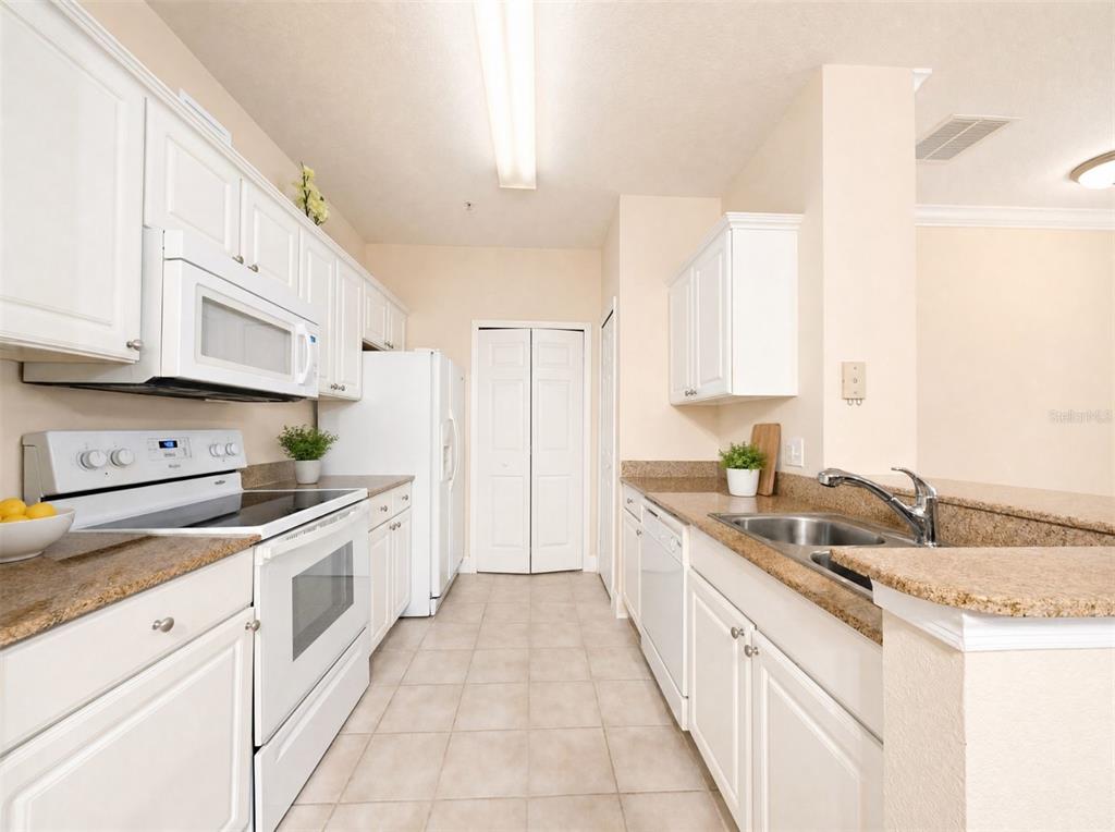 A galley-style kitchen features white cabinets, granite countertops, white appliances, and light-colored tile flooring — 143 SOUTHERN PECAN CIRCLE UNIT 201, WINTER GARDEN, FL