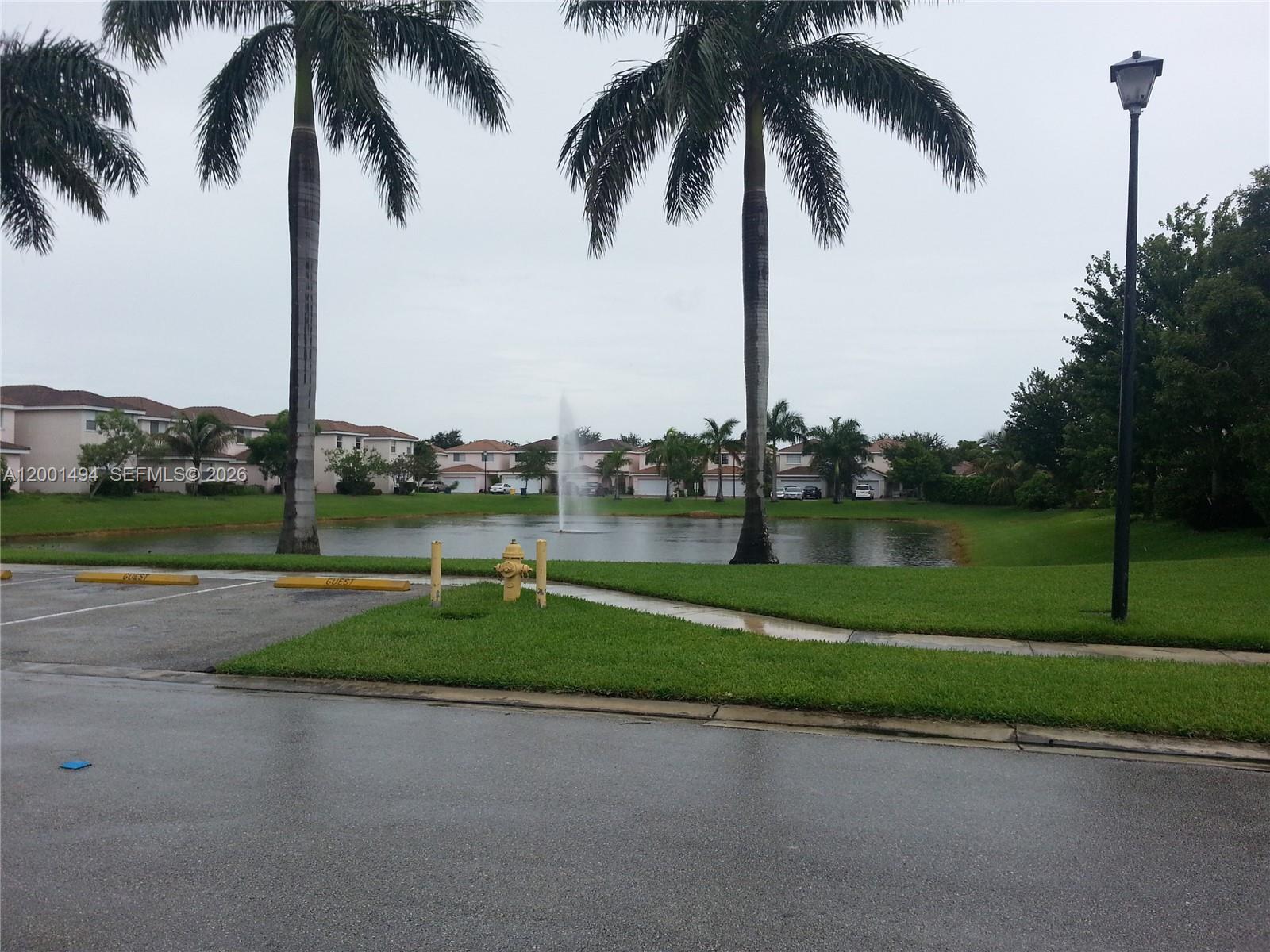 A view of a pond with a fountain, palm trees, and residential buildings in the background — 5450 NW 94th Ter, Sunrise FL 33351, SUNRISE, FL