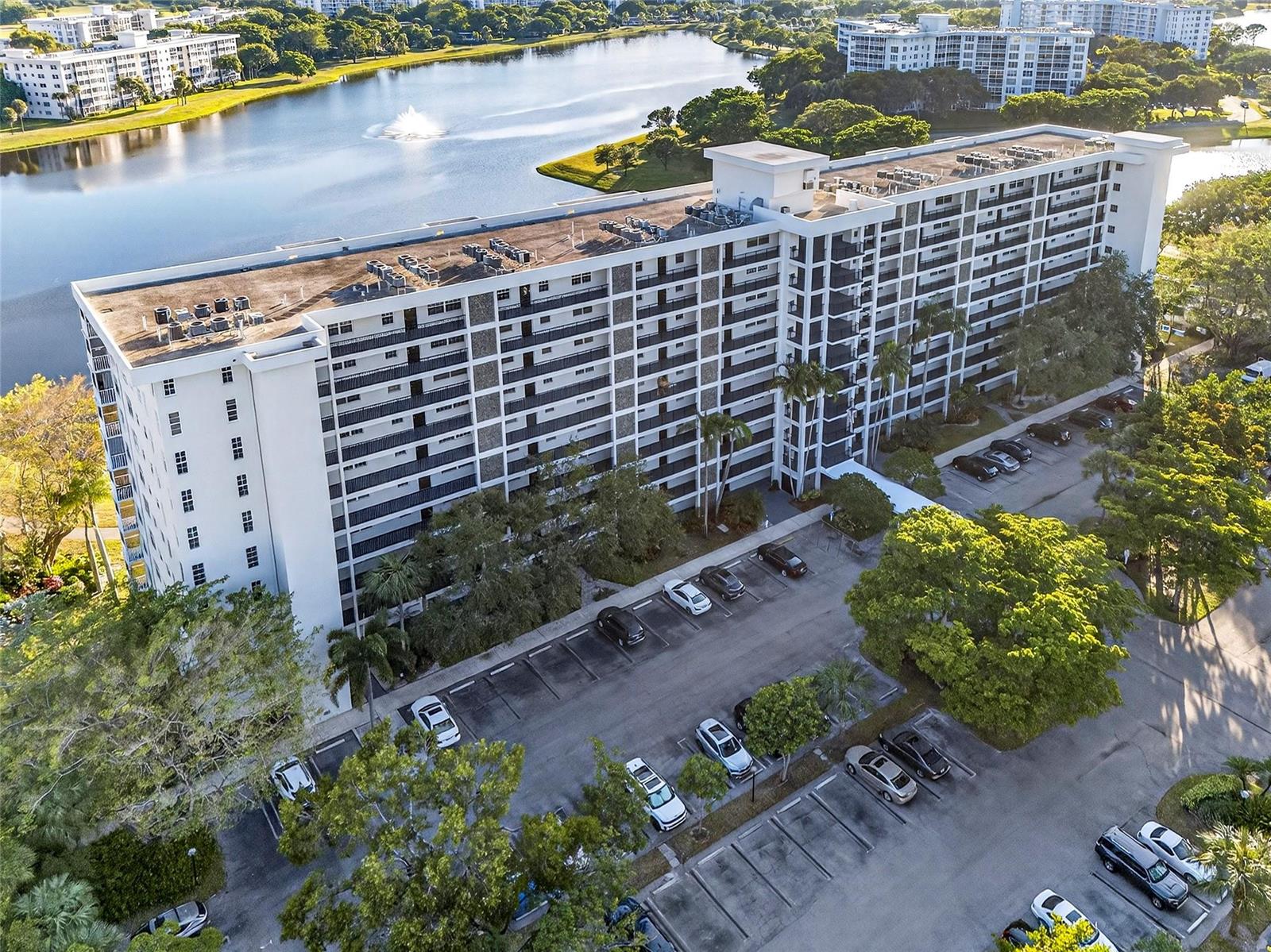 An aerial view shows a multi-story apartment building beside a lake with a parking lot — 2900 N Course Drive # 607, Pompano Beach FL 33069, POMPANO BEACH, FL