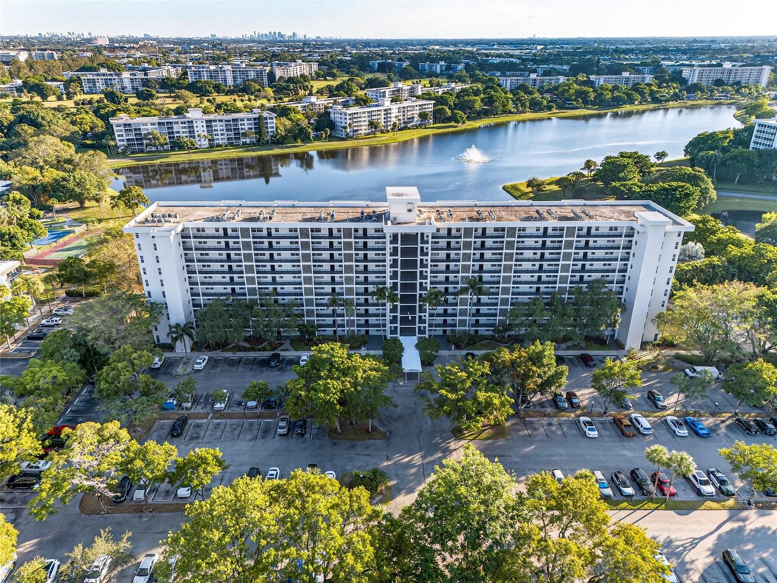 An aerial view shows a multi-story apartment building situated beside a lake and parking lot — 2900 N Course Drive # 607, Pompano Beach FL 33069, POMPANO BEACH, FL
